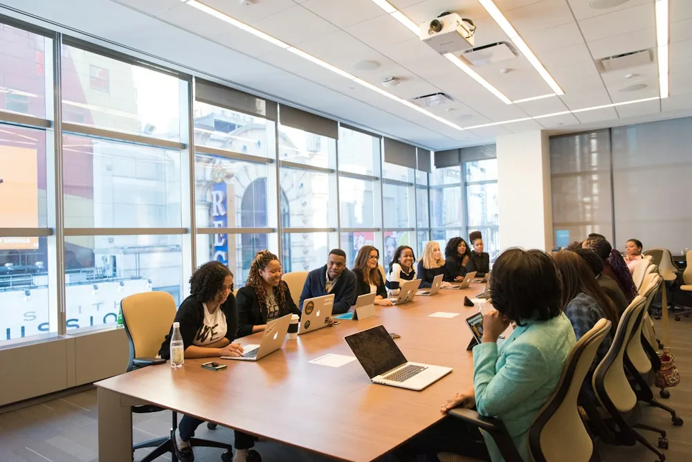 A group seated around a long boardroom table with laptops
