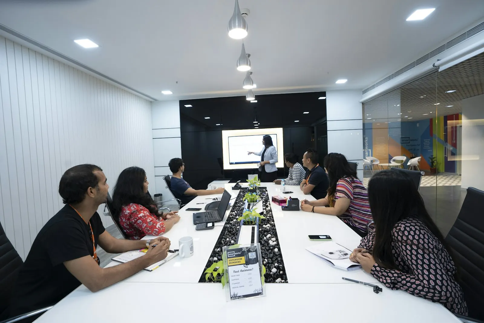 A team seated at a long table listening to a colleague presenting